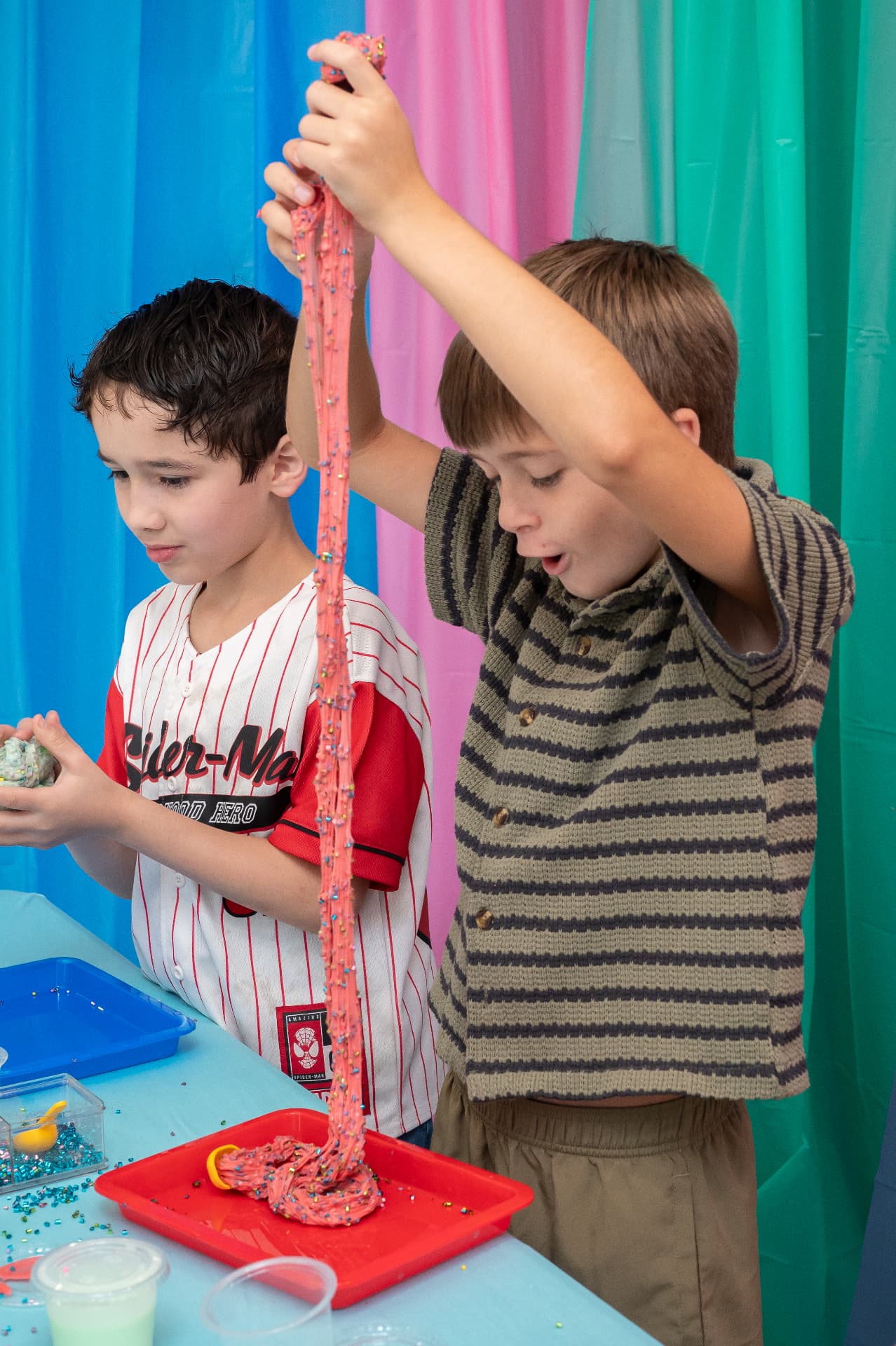 Two boys stretching pink slime together at a party